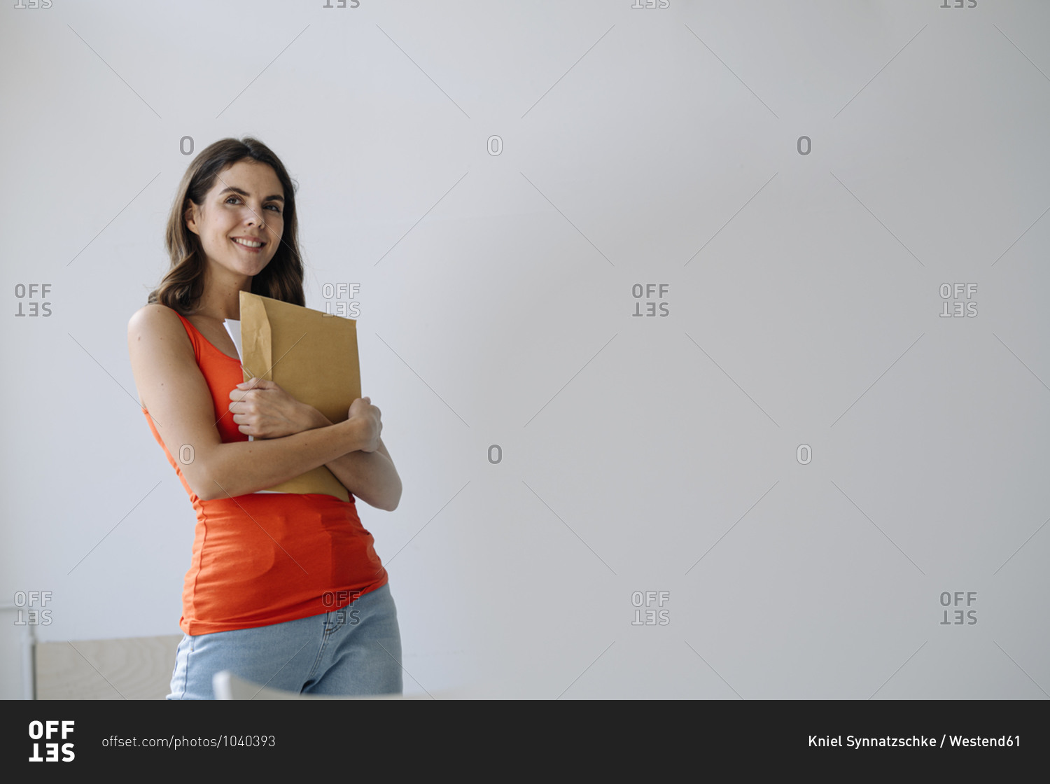 Woman holding paper in hand while standing against white wall at home