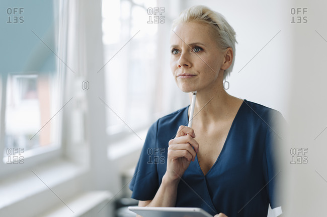 Thoughtful businesswoman holding digital tablet and digitized pen in office seen through glass