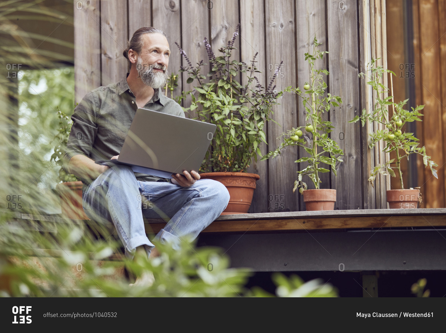 Thoughtful bearded man with laptop sitting outside tiny house