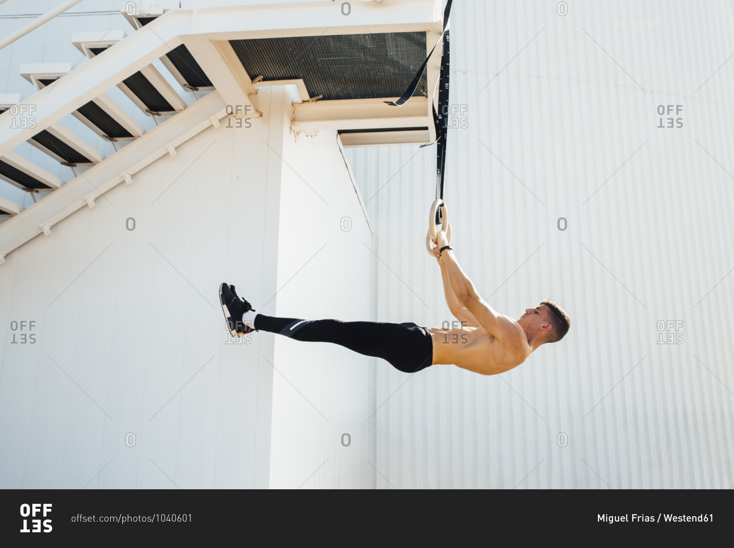 Athlete balancing body weight while hanging on ring at staircase outdoors