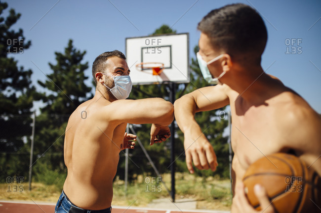 Men with face mask greeting with elbow bump at basketball court