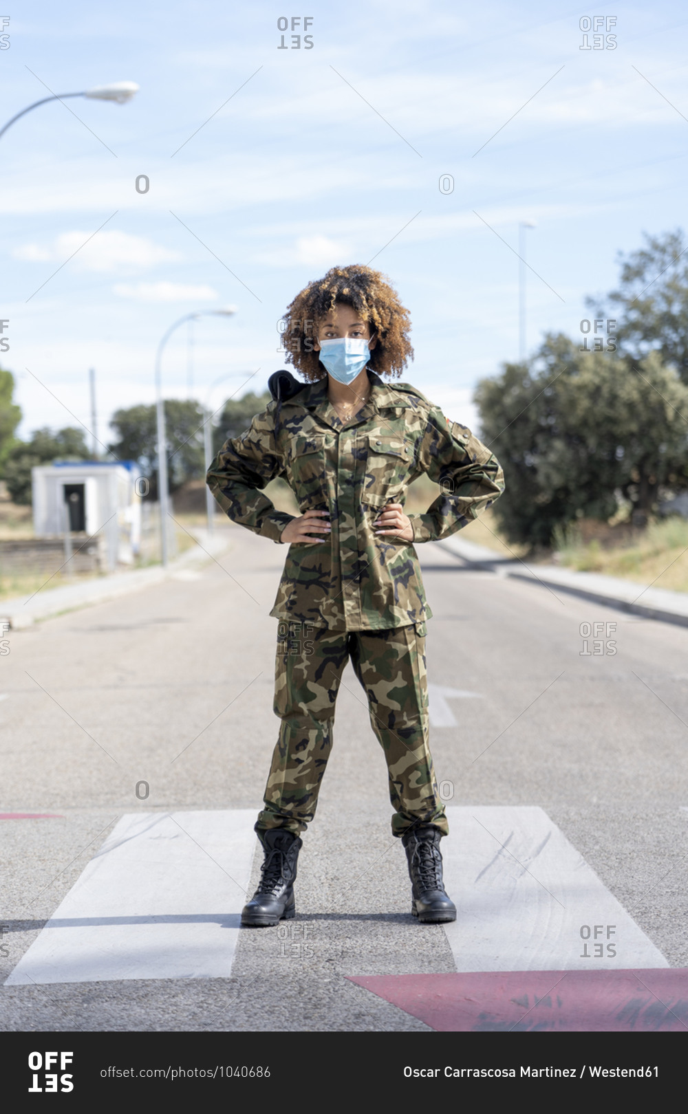 Female army soldier wearing protective face mask with hands on hip standing on street