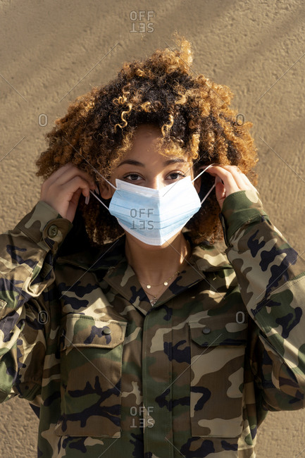 Female military officer wearing protective face mask while standing against wall