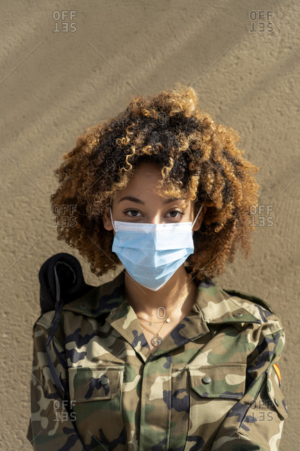 Female army soldier with protective face mask while standing against wall