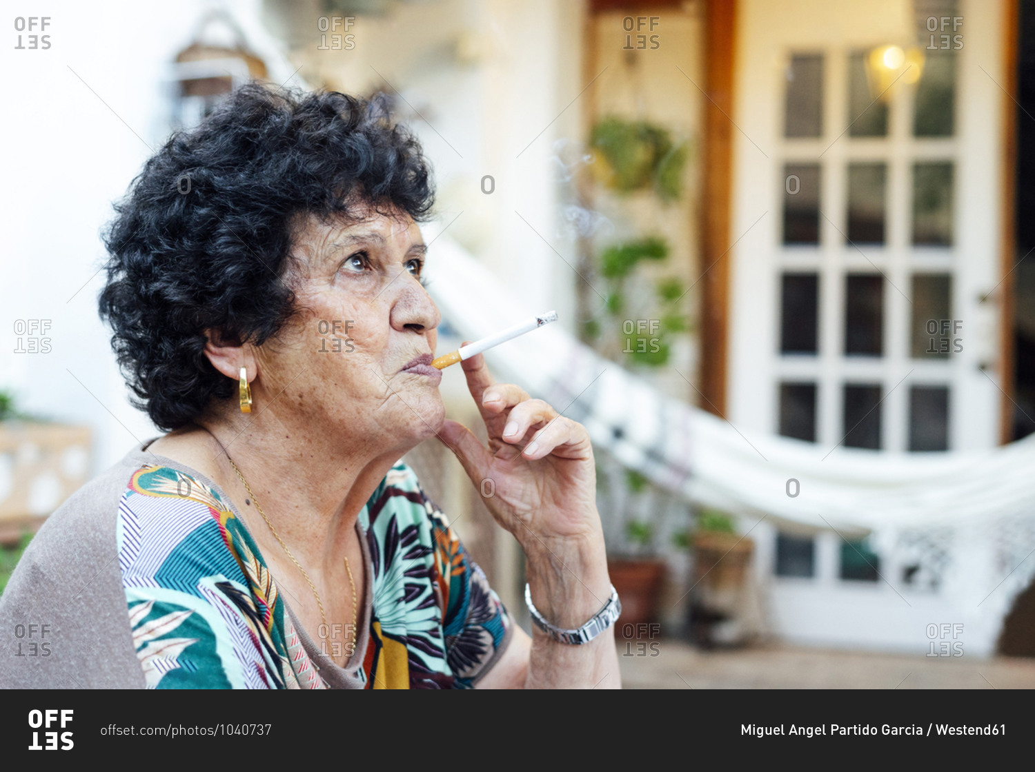 Close-up of senior woman smoking cigarette while sitting outside house in yard