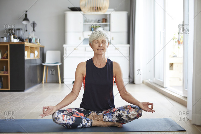 Active senior woman meditating on exercise mat at home