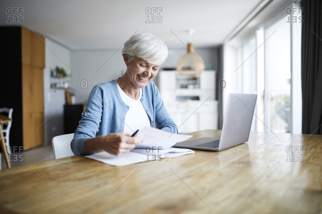 Smiling active senior woman doing paper work while sitting at home