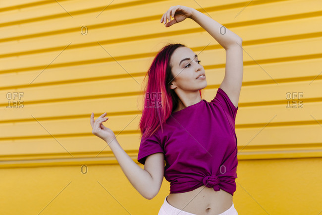 Young woman with dyed hair looking away while dancing against yellow wall
