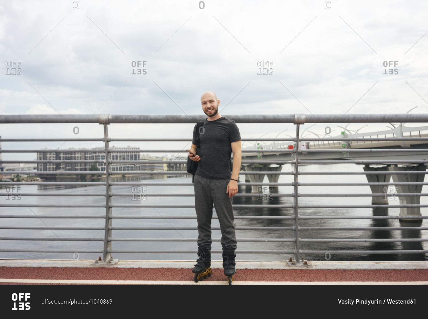 Smiling young man with inline skates using smart phone while standing on bridge