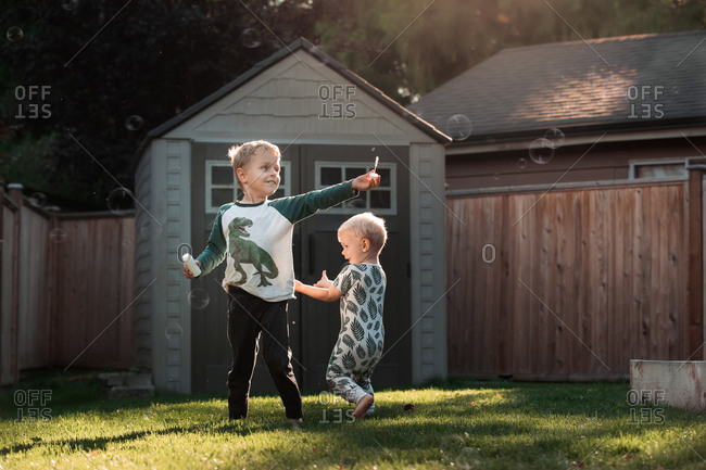Two little boys playing with bubbles at sunset in the backyard