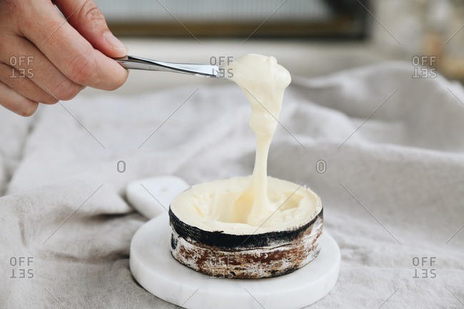 Hand dipping knife in a spruce bark banded gooey cheese dip on marble