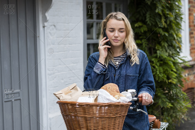Young blond woman on bicycle with basket, talking on mobile phone.