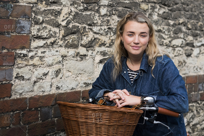 Young blond woman on bicycle with basket, looking at camera.