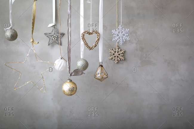 Christmas decorations, close up of silver, white and golden Christmas baubles on ribbons on grey background.