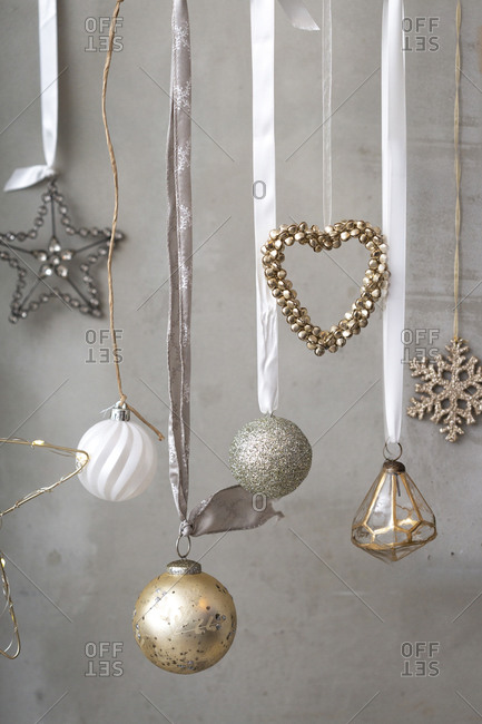 Christmas decorations, close up of silver, white and golden Christmas baubles on ribbons on grey background.