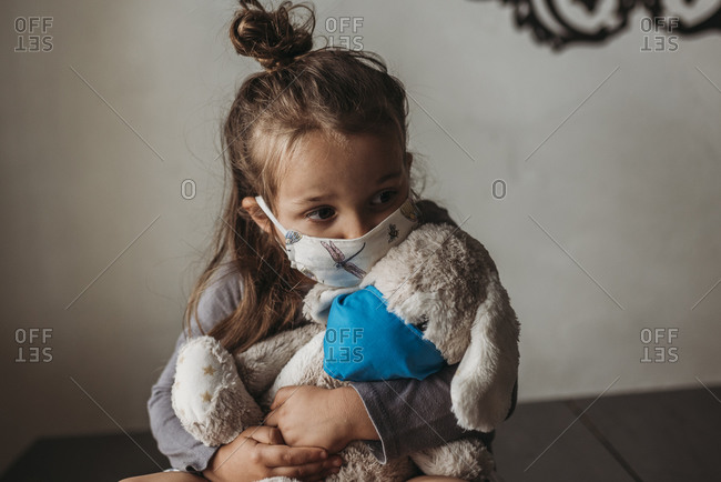 Close up of young girl with mask on kissing masked stuffed animal
