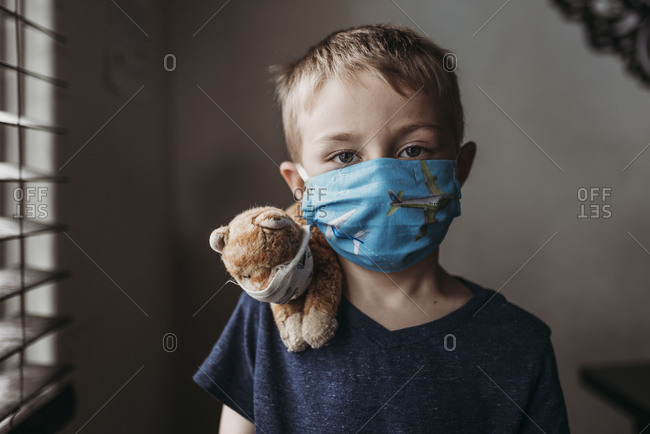 Close up of young school aged boy with mask on with stuffed animal