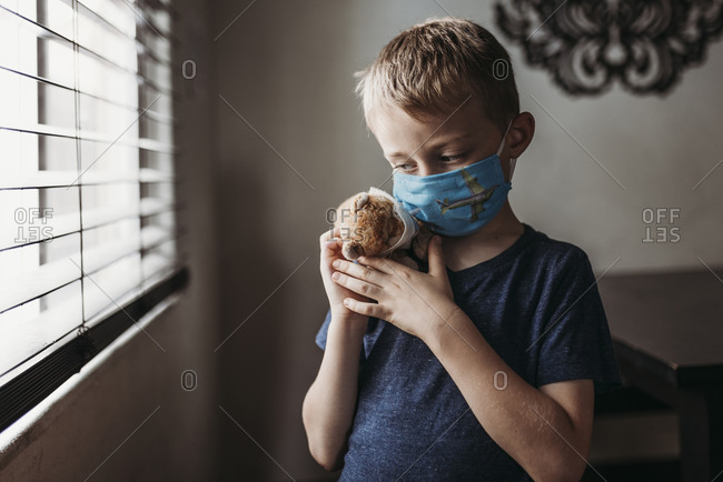Close up of young school aged boy with mask on with stuffed animal