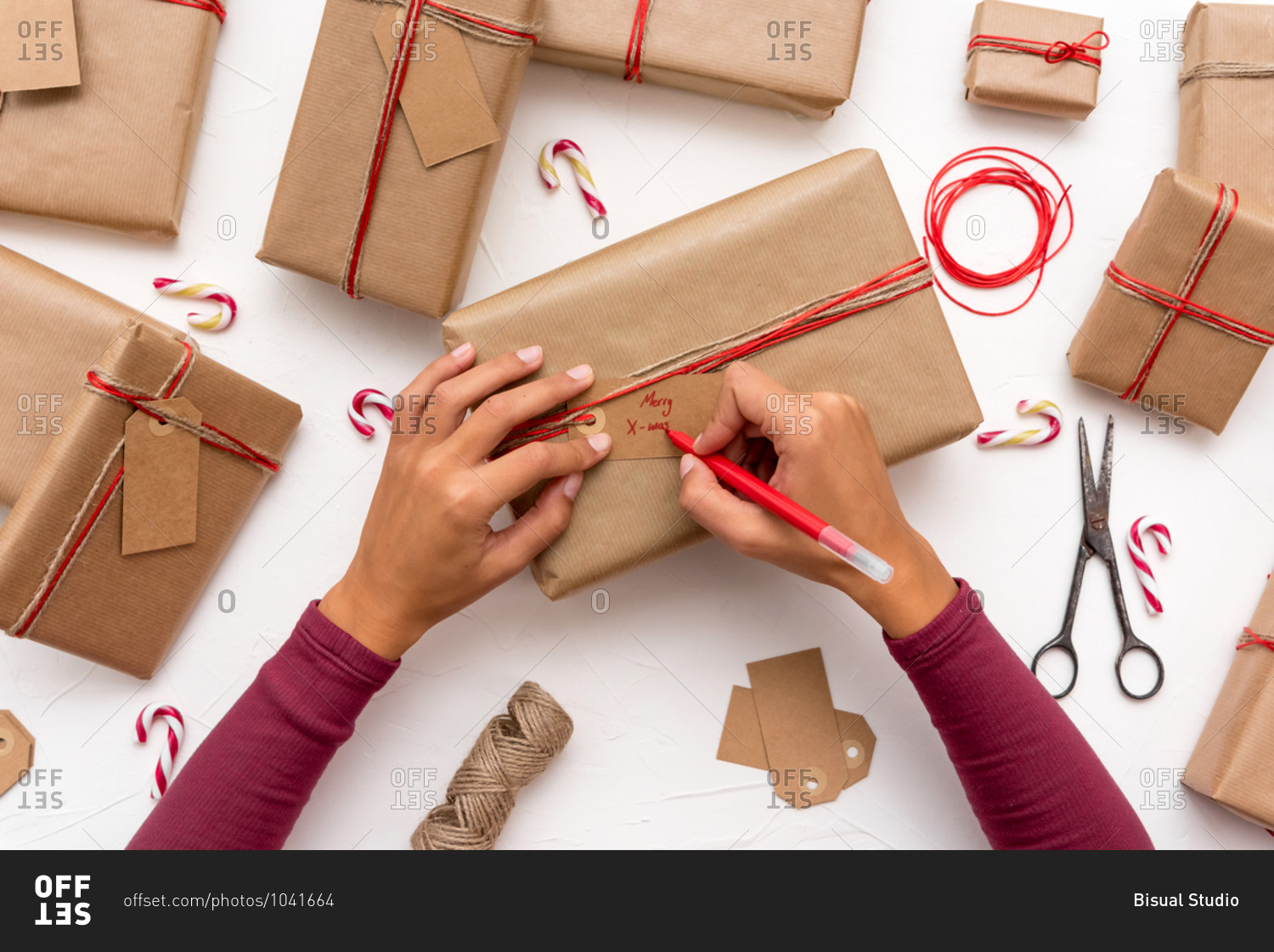 Female's hands writing Christmas cards on gift boxes decorated with kraft paper