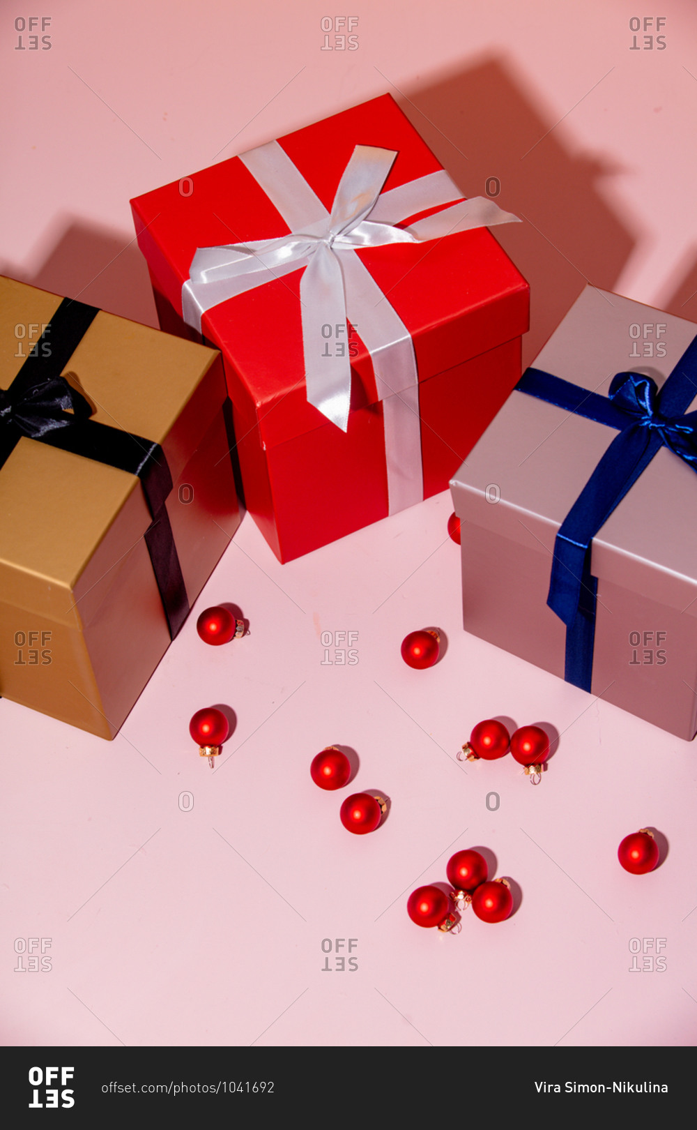 Overhead view of three holiday boxes and Christmas baubles on a pink table