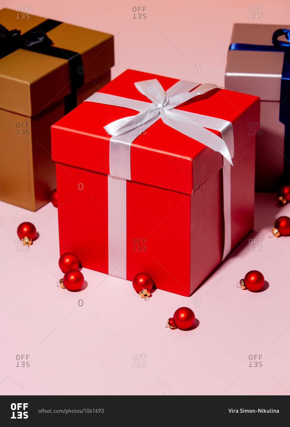 Three holiday boxes and Christmas baubles on a pink table