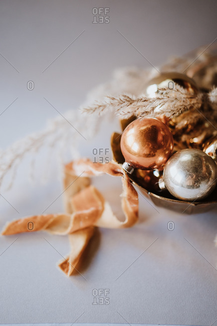 Close up of gold and silver Christmas ornaments with organic materials in bowl on white surface