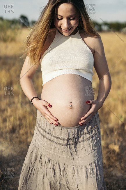 Pregnant woman touching her belly and looking down in the countryside.