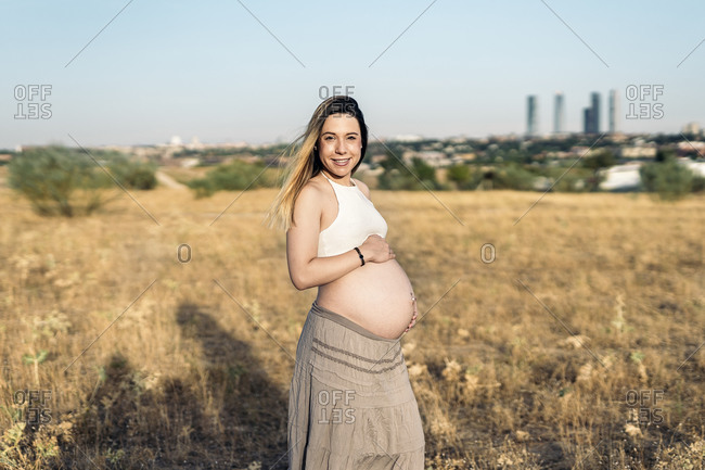 Pregnant woman touching her belly and looking at camera.
