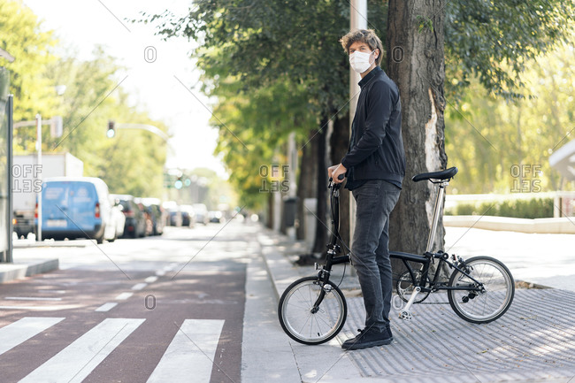 Handsome man wearing face mask using his detachable bike in the street.