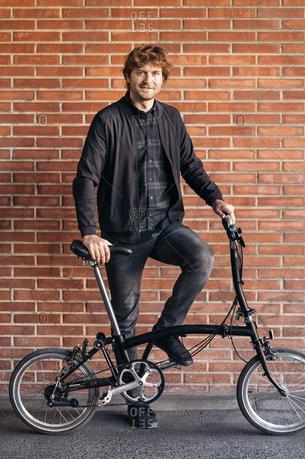 Handsome man standing and looking at camera next to his detachable bike.