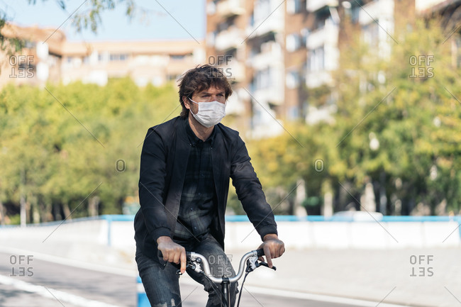 Handsome man wearing face mask using his detachable bike in the street.