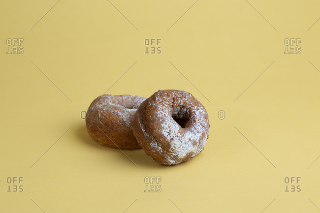 Two Doughnuts with Powdered Sugar on Yellow Background