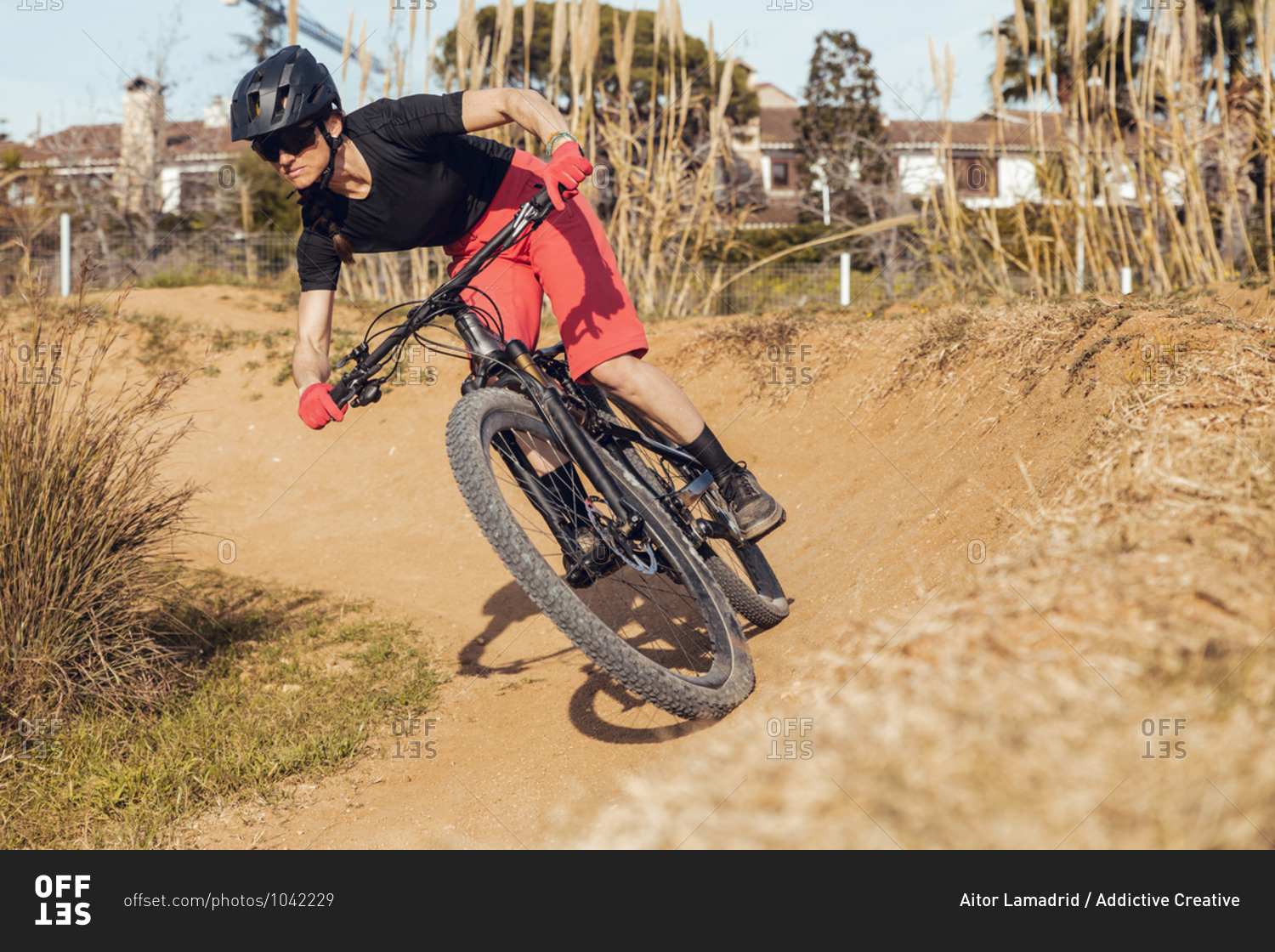 Sportswoman in black helmet and red sportswear with glasses riding mountain bike on training track