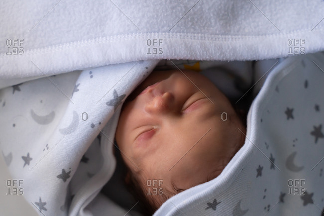From above close up view of adorable tiny newborn child wrapped in blanket sleeping peacefully in crib
