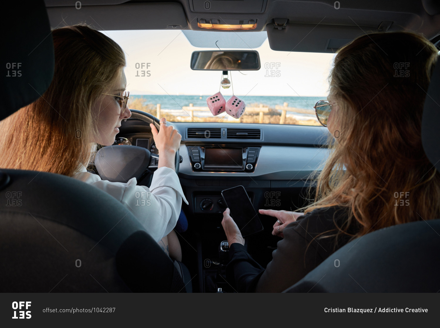 Back view of traveling women sitting in modern automobile and checking route on smartphone while navigating on online map during road trip