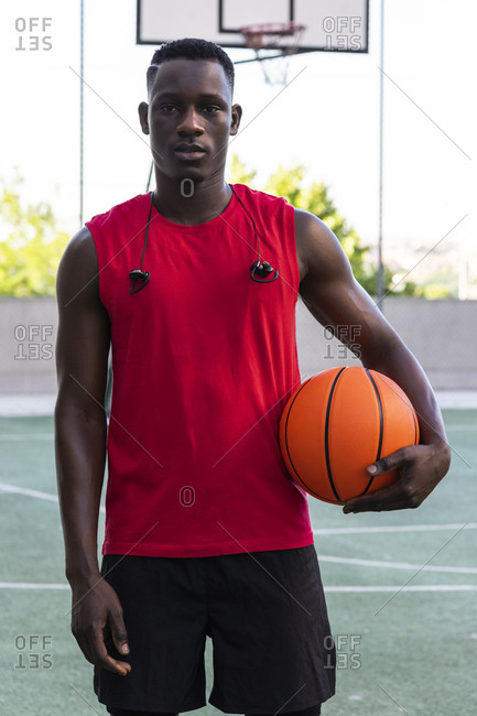 Determined male basketball player standing with ball on playground in summer and looking at camera