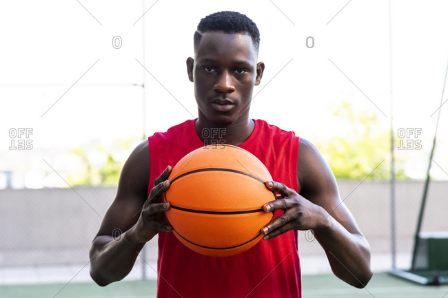 Determined male basketball player standing with ball on playground in summer and looking at camera