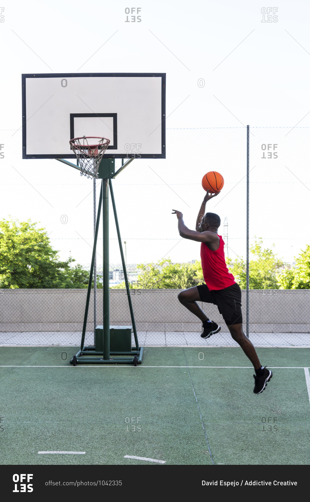 Side view of African American sportsman jumping above ground while playing basketball during training and throwing ball into hoop
