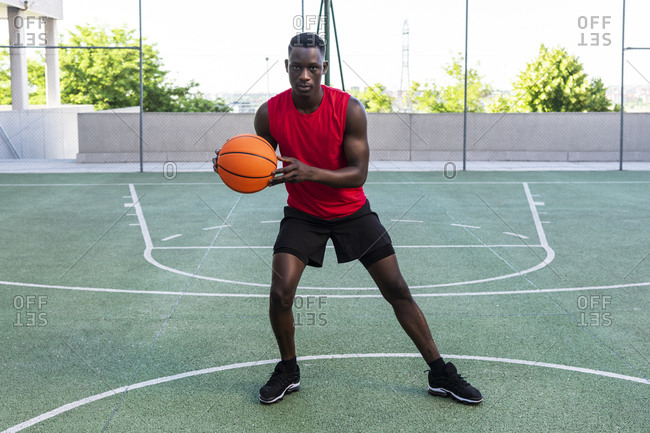 Serious African American male playing basketball on modern sports ground and looking at camera during training