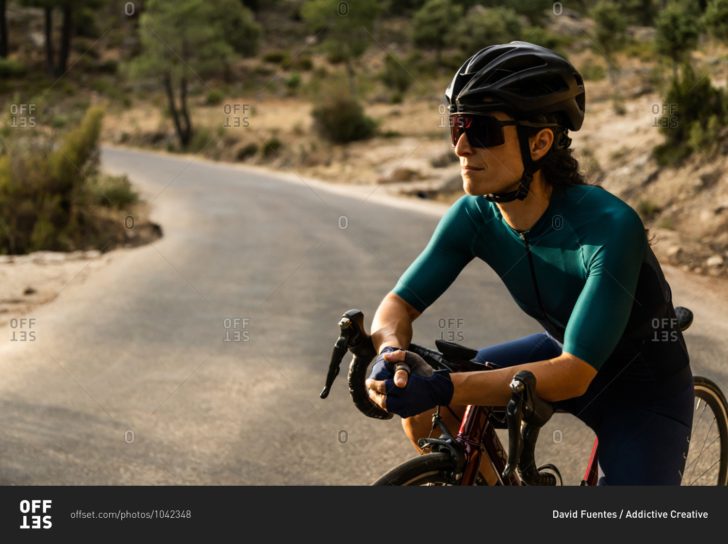 mature woman training road bike, climbing a mountain road, resting sit on the bike, side view