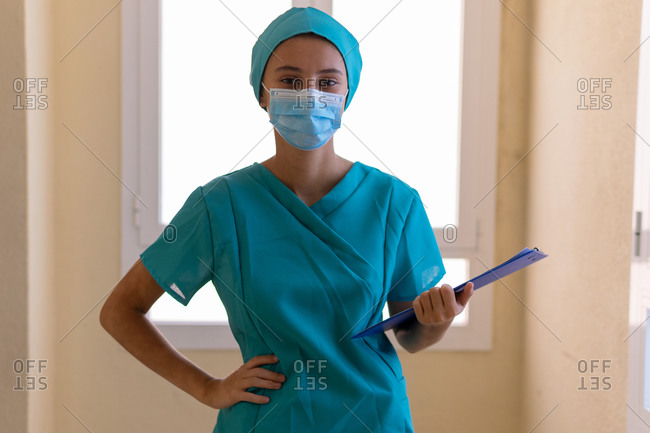 Concentrated young nurse in blue uniform and mask with clipboard while working in hospital