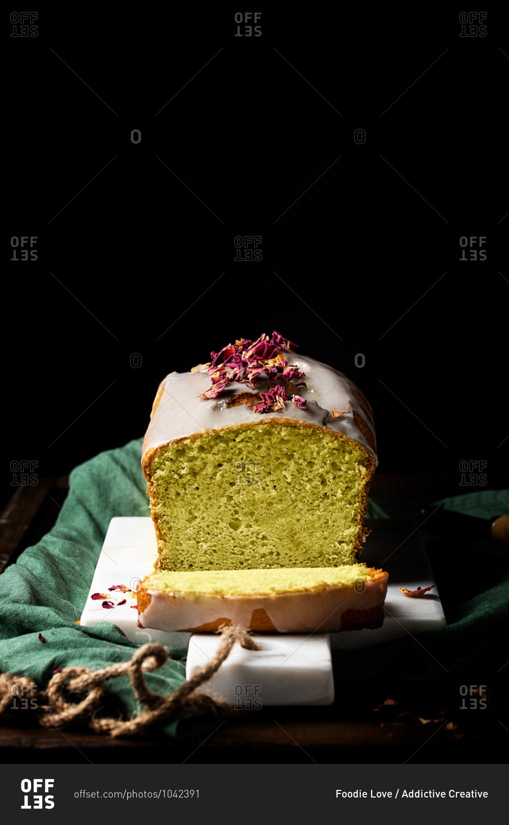 Tasty homemade cake with glaze and flower petals served on plate on table in studio on black background