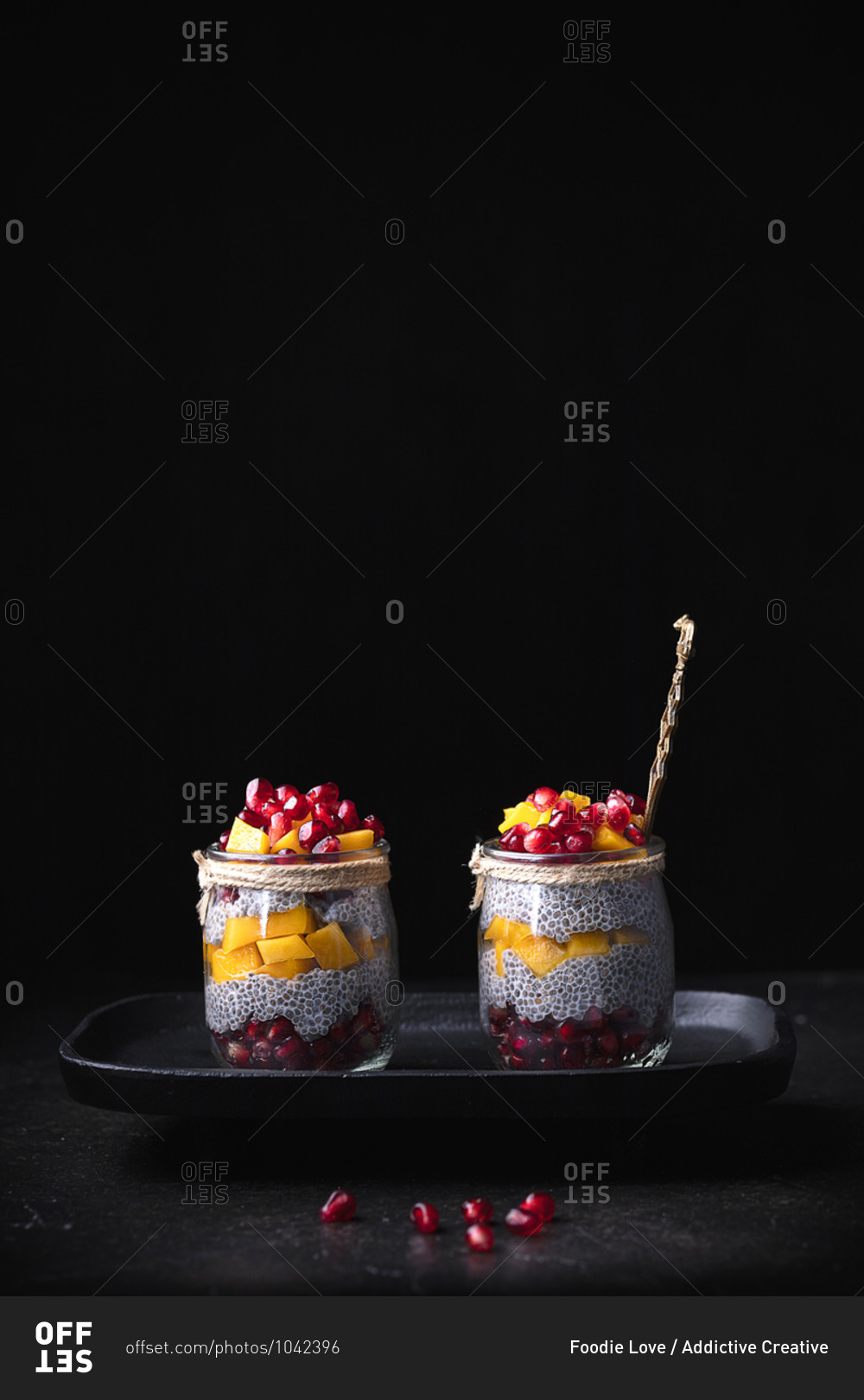 Glass jars with various tropical fruits placed on tray on table on black background in studio