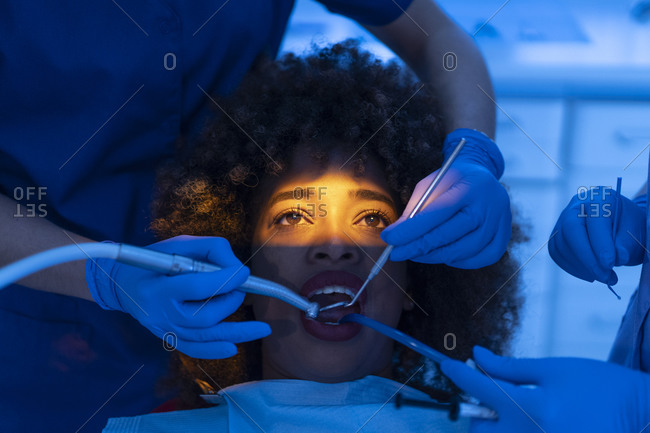 Crop of dentist and assistant using dental suction device on teeth of black woman in clinic