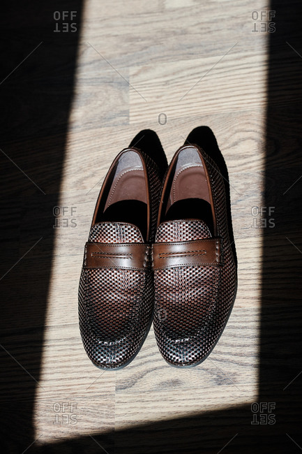 Pair of leather loafers placed on wooden floor illuminated by sunlight in room of modern apartment