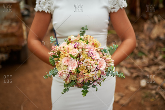 Cropped unrecognizable bride in elegant white dress standing with bouquet of delicate flowers in a outdoor garden on wedding day