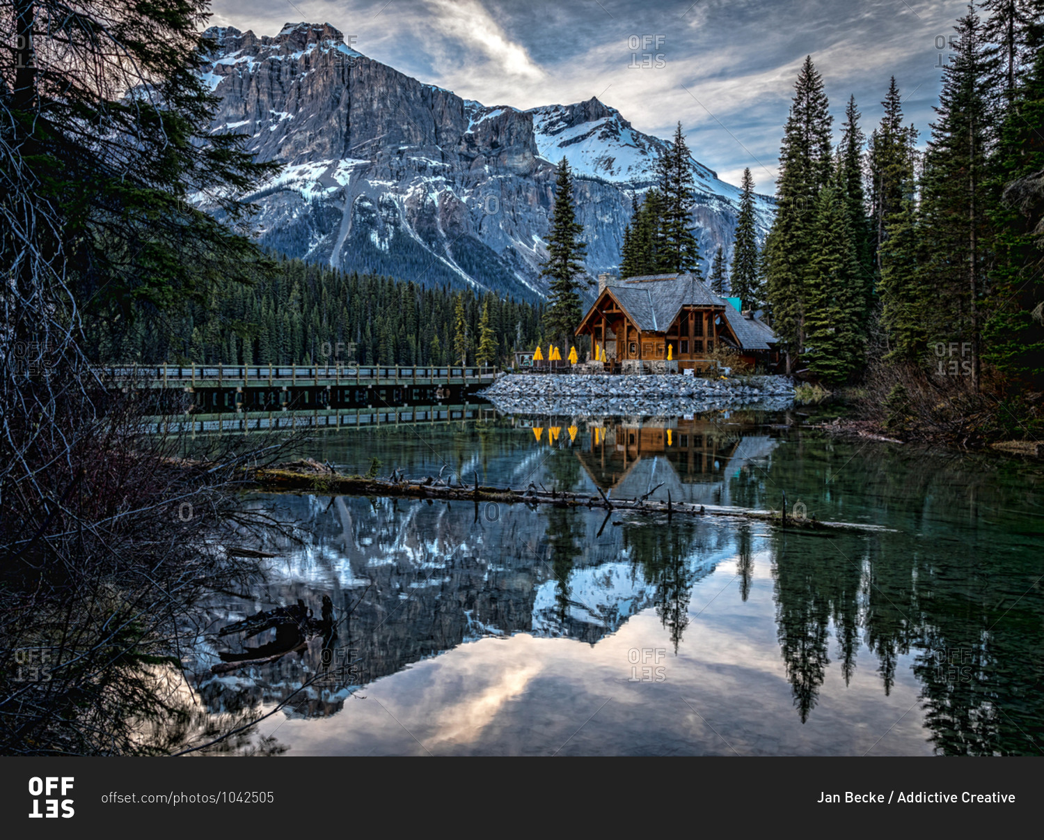 Magnificent scenery of Emerald Lake with bridge over water and wooden house on shore surrounded by green pine forest against rocky mountains covered with snow in Yoho National Park in Canada