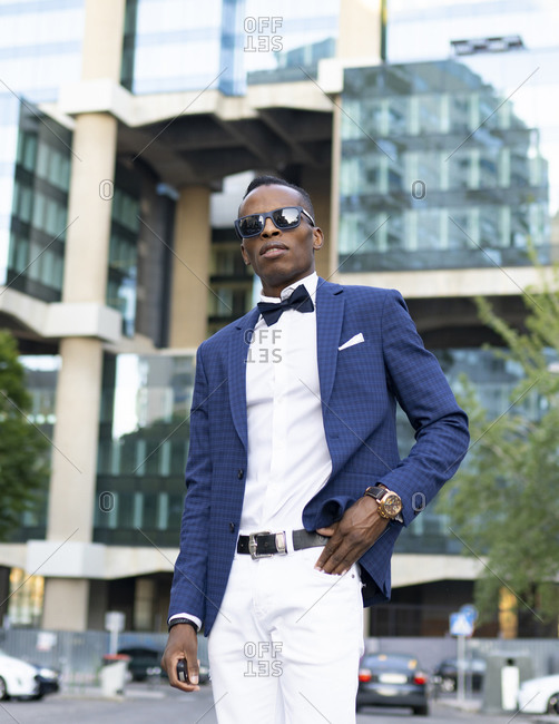 Low angle of masculine African American male entrepreneur wearing elegant suit and sunglasses standing in city