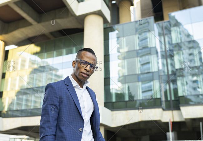 Low angle of masculine African American male entrepreneur wearing elegant suit standing in city and looking at camera