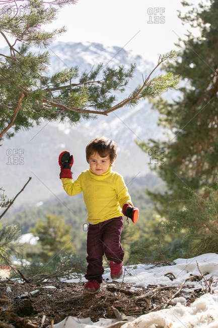 Cute kid in warm clothes walking on hill in highlands in winter while looking away
